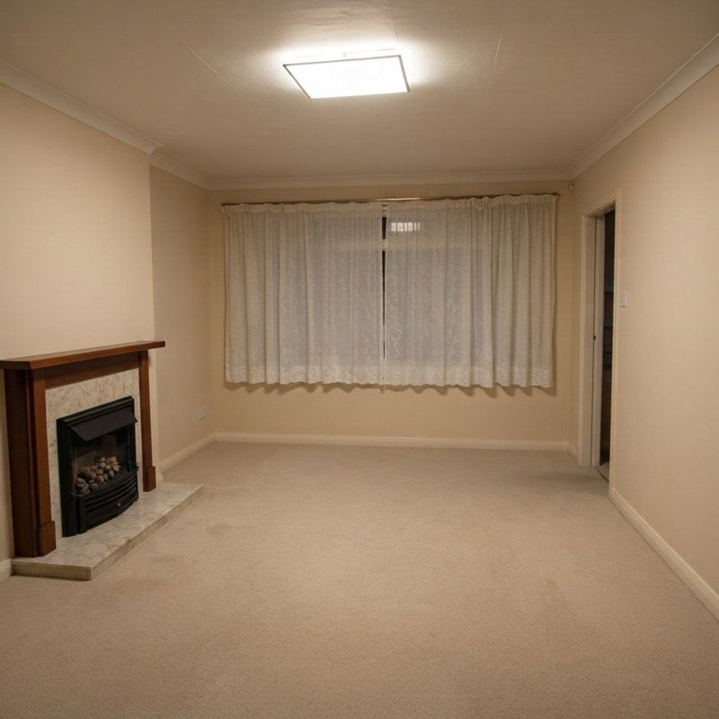 The same living room with all the furniture and wall pictures removed, leaving the fireplace, curtains and carpet.